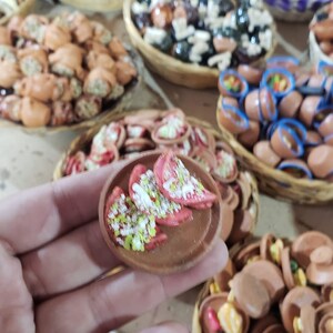 Puede incluir: Un primer plano de un peque&ntilde;o plato de cer&aacute;mica pintado a mano con un dise&ntilde;o rojo y blanco. El plato est&aacute; lleno de peque&ntilde;as piezas de cer&aacute;mica blancas y verdes. El plato est&aacute; siendo sostenido en la mano de una persona.