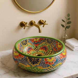 May include: A decorative, round ceramic sink with a vibrant floral pattern in red, yellow, and blue. The sink has a green rim and is set on a marble countertop. Gold-colored faucet fixtures and a mirror are visible.