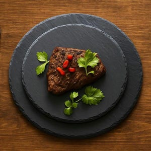 Puede incluir: Un filete cocido sobre tres fuentes negras de pizarra. Adornado con perejil verde fresco y chiles rojos. Las fuentes están dispuestas sobre una superficie de madera.