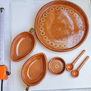 May include: Set of six terracotta pottery dishes, including a large serving platter with a white and green dot pattern, two small bowls, two small spoons, and a large, leaf-shaped dish.
