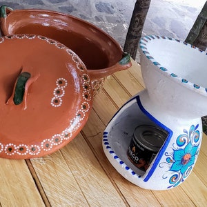 May include: Two terracotta pots, one with a lid and the other with a decorative floral design. The pot with the lid has white and green dots around the rim. The other pot has a blue and green floral design and a small metal container inside.