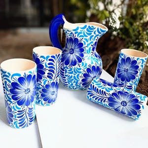 Puede incluir: Un juego de cuatro tazas de cerámica azul y blanca y una jarra a juego con diseños florales. Las tazas y la jarra están pintadas a mano con detalles intrincados.