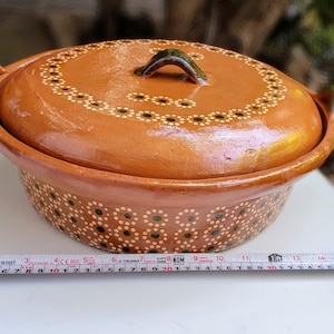 May include: A terracotta casserole dish with a lid, featuring a black and white dot pattern. The dish is approximately 11 inches in diameter.