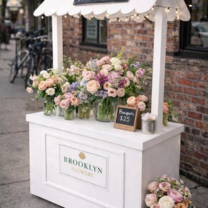 Peut inclure: Un étal de fleurs blanc avec un toit festonné présente des bouquets de fleurs fraîches dans des bocaux en verre. L'enseigne indique "Fresh Flowers" et "Brooklyn Flowers". Un petit tableau noir indique le prix des bouquets.