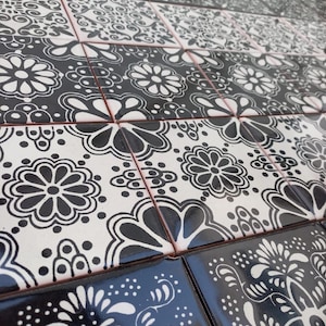May include: Black and white patterned ceramic tiles with intricate floral designs. The tiles are arranged in a staggered pattern, creating a visually appealing mosaic.