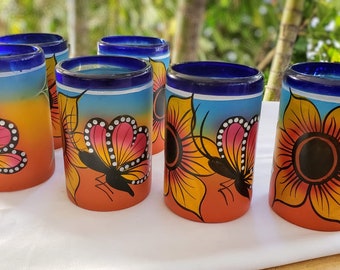 Puede incluir: Juego de seis vasos de chupito de vidrio coloridos con bordes azules. Cada vaso presenta un diseño diferente pintado a mano de una mariposa y una flor en tonos naranja, amarillo, rosa y azul.