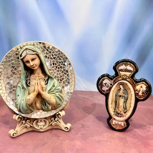 Puede incluir: Dos figuras religiosas, una de la Virgen María con un fondo de mosaico y la otra una cruz con cuatro imágenes de la Virgen María. Ambas figuras son blancas con detalles dorados.
