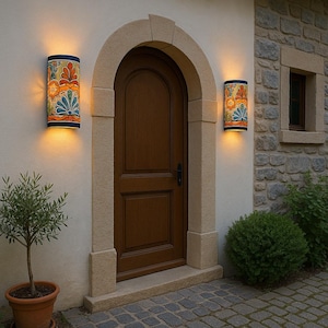 May include: Two cylindrical outdoor wall sconces with colourful floral patterns flank a wooden door. The sconces have a dark blue top and bottom, and the floral design includes orange, blue, and green elements. The door is framed by a stone arch.