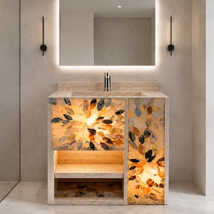 Puede incluir: Un mueble de baño con encimera de piedra, lavabo integrado y grifo cromado. Los paneles frontales están decorados con un mosaico retroiluminado de piezas de piedra translúcidas en forma de hoja de colores ámbar, marrón y gris.