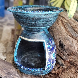 May include: A blue ceramic oil burner with a white and blue floral design. The burner has a small opening on the side for adding oil and a larger opening on the top for placing a tea light.