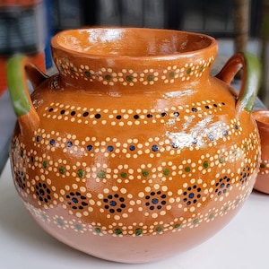 May include: A brown clay pot with green and black painted dots. The pot has two handles and a wide opening.
