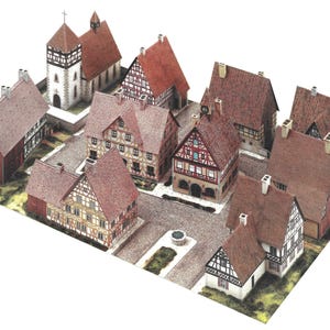 Könnte beinhalten: Ein Miniaturmodell eines europäischen Dorfes mit mehreren Gebäuden mit roten Ziegeldächern und Fachwerkwänden. Eine Kirche mit Turm und ein kleiner Brunnen sind ebenfalls zu sehen. Das Modell steht auf einer grün-grauen Basis.