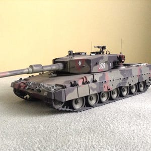 Puede incluir: Maqueta detallada de un tanque en colores de camuflaje verde, marrón y rojo. El tanque tiene un cañón largo y múltiples ruedas. El número "0227" es visible en el lateral del tanque.