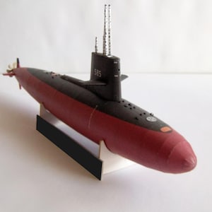 May include: A model submarine with a red hull and black upper section. The model has a conning tower with the number 585, and two vertical masts. The submarine rests on a white and black stand.