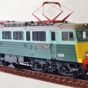 Puede incluir: Una maqueta de locomotora eléctrica, pintada en tonos verdes, azules y amarillos, se encuentra sobre una vía marrón. La locomotora presenta el número EU07-541 y un pantógrafo rojo. El modelo es una representación detallada de un tren polaco PKP.