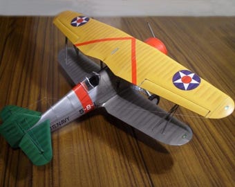 May include: A yellow and gray model airplane with red accents and a US Navy insignia. The plane has a star on the wing and the number 5-B on the side.