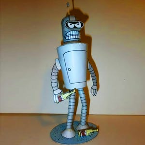 May include: A handmade papercraft figure of Bender from Futurama. The robot is gray and white with a silver body, a door, and a menacing expression. He holds a beer bottle and has another on the ground.