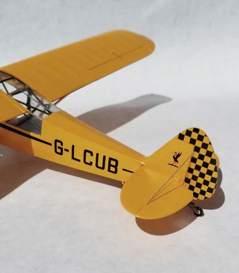 Puede incluir: Un modelo de avi&oacute;n amarillo con cola a cuadros blancos y negros y el texto "G-LCUB". El avi&oacute;n tiene una envergadura de aproximadamente 25 cm. El modelo es una r&eacute;plica de un avi&oacute;n antiguo.