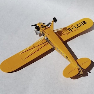 Puede incluir: Un modelo de avi&oacute;n amarillo con h&eacute;lice negra y detalles de cola. Las alas est&aacute;n etiquetadas con el texto "G-LCUB". El modelo tiene un dise&ntilde;o cl&aacute;sico, con una peque&ntilde;a cabina y puntales que sostienen las alas.