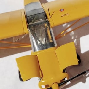 Puede incluir: Maqueta detallada de avi&oacute;n en amarillo brillante, con cabina transparente y h&eacute;lice en blanco y negro. Las alas y el fuselaje son de color amarillo liso, con detalles visibles como la cola y el tren de aterrizaje. El modelo es una r&eacute;plica en miniatura.