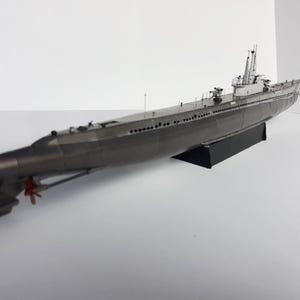 May include: A detailed model of a submarine, primarily gray with white accents on the conning tower. The model sits on a black stand, showcasing the propeller and hull details. The submarine model is a collectible item.