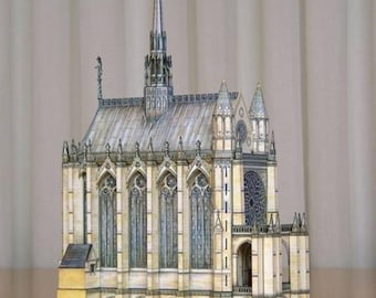 May include: A detailed paper model of a medieval chapel with a tall spire, intricate stonework, and stained glass windows. The model is made of paper and is painted in shades of gray, white, and yellow.