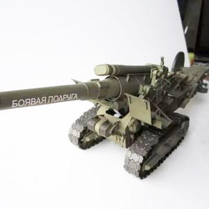 Puede incluir: Un modelo verde de un cañón de artillería militar con un cañón largo y orugas. El cañón tiene el texto "БОЙВАЯ ПОДРУГА" escrito en el cañón.