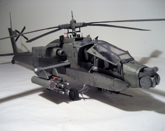May include: A detailed model of a military helicopter, painted in a camouflage pattern. The helicopter has a clear cockpit, a rotating blade, and a set of rockets attached to the side.