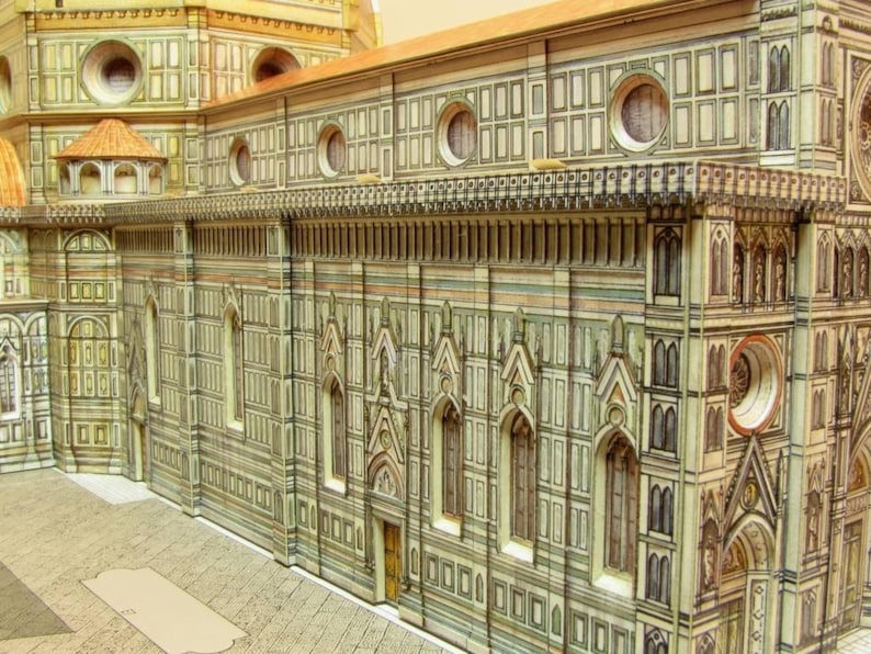May include: A detailed model of a large, ornate building with a white and beige facade. The building has many windows and arches, and is decorated with intricate carvings. The model is made of paper or cardboard and is very realistic.