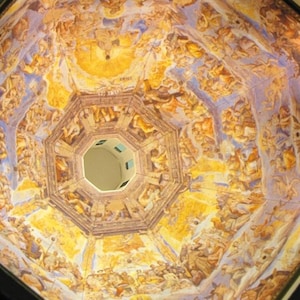 May include: A close-up view of a painted ceiling with a circular opening in the centre. The ceiling is painted in shades of yellow, blue, and white, with intricate details and figures. The circular opening reveals a glimpse of the sky.