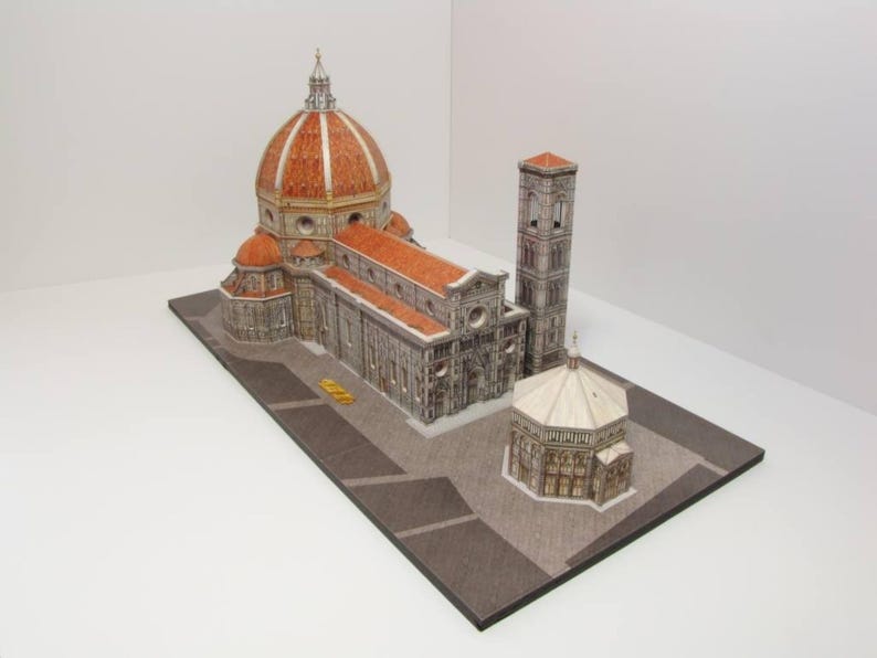 May include: A detailed model of the Florence Duomo, a famous Italian cathedral, with a red tiled roof, a large dome, and a bell tower. The model is made of paper and is displayed on a brown base.