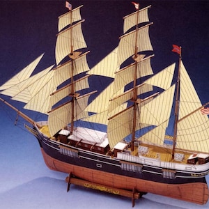 May include: A detailed model of a tall ship with multiple masts and sails. The ship features a black hull with a red lower section and cream-colored sails. Small American flags are visible on the masts. The model is displayed on a wooden stand.