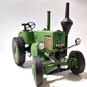 Może przedstawiać: Zielony model traktora z czarnymi oponami, czarnym kominem i małą kierownicą. Traktor ma napis "URSUS B45-853" z przodu. Jest to miniaturowa replika.