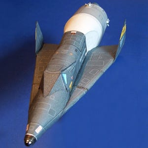 May include: A detailed model of a spacecraft, primarily gray with white and silver accents. The design features a cylindrical body and angled wings. The model is set against a solid blue background, showcasing its intricate construction.