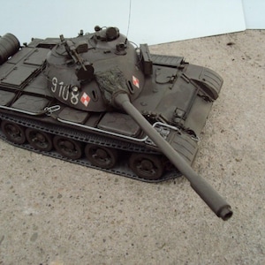 May include: A detailed model of a military tank in olive green. The tank has a long gun barrel, a rotating turret, and visible tracks. The number "9108" is painted on the side, along with a red and white emblem. The tank is a collectible item.