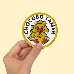 May include: Yellow embroidered patch with a cartoon yellow chick with orange feet and the text "Chocobo Tamer" in black.