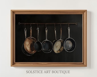 Puede incluir: Pintura enmarcada que presenta una colección de sartenes de cobre y acero inoxidable colgadas sobre un fondo negro. Las sartenes están suspendidas de una barra horizontal. El marco es de madera. El texto "SOLSTICE ART BOUTIQUE" está en la parte inferior.