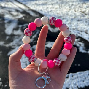 May include: Pink and white checkered silicone beaded keychain with a silver key ring. The beads are interspersed with white beads that have small rhinestones.