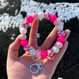 May include: Pink and white beaded keychain with a checkered pattern and a silver clasp.