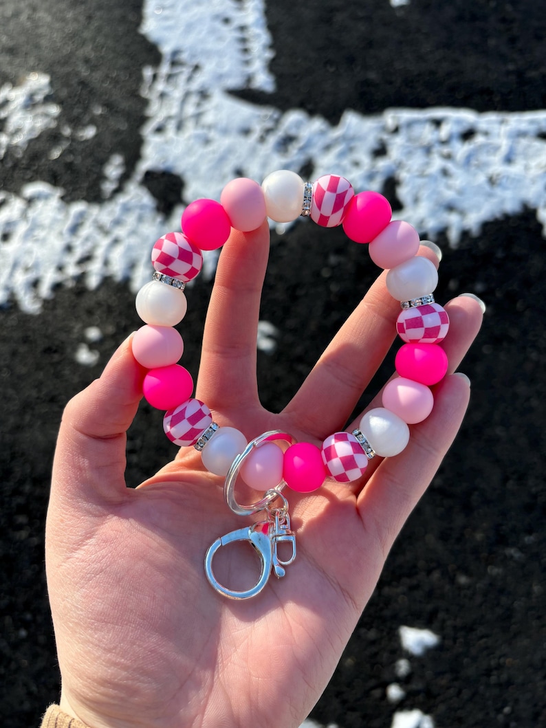 May include: Pink and white beaded keychain with a checkered pattern and a silver clasp.