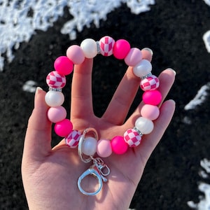 May include: Pink and white checkered silicone beaded keychain with a silver key ring. The beads are interspersed with white beads that have small rhinestones.