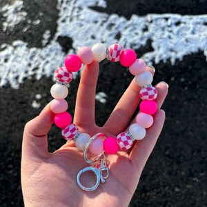 May include: Pink and white silicone beaded keychain with a checkered pattern and silver key ring.
