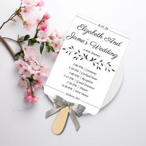 Könnte beinhalten: Ein weißer Hochzeitfächer mit schwarzem Text und einem floralen Design. Der Text lautet "Elizabeth and James' Wedding, a new journey" und enthält den Zeitplan für die Hochzeitszeremonie und den Empfang.