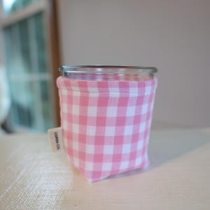 May include: A clear glass jar with a pink and white gingham fabric cozy. The cozy has a small tag that reads "COREN CO." The jar is sitting on a white surface.