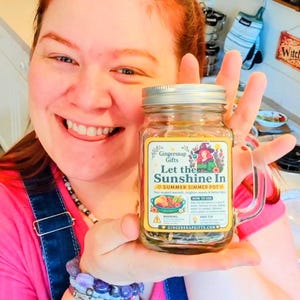 May include: A clear glass jar with a silver metal lid and a handle, containing dried ingredients for a simmer pot. The label features the text Gingersnap Gifts, Let the Sunshine In, Summer Simmer Pot, and instructions for use, with a colorful illustration.