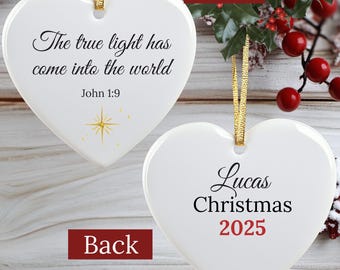 May include: White heart-shaped Christmas ornament with gold ribbon. The front has the text "The true light has come into the world" and "John 1:9". The back says "Lucas Christmas 2025".
