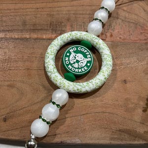 May include: A white and green beaded keychain with a circular charm featuring a green and white design and the text "NO COFFEE WORKEE". The charm has a green image of a character. The keychain has white beads with green accents.