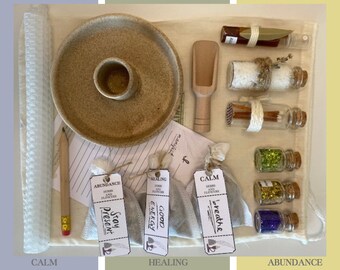 May include: A white cloth bag filled with various items, including small glass bottles, pouches, and a ceramic dish. The items are labelled with words like "Calm", "Healing", and "Abundance".