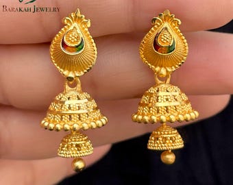 May include: Gold-toned dangle earrings with a bell-shaped design. The earrings feature intricate detailing and a small, colorful accent at the top. The earrings are from Barakah Jewelry.