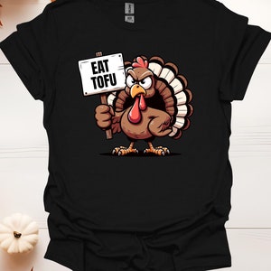 Puede incluir: Camiseta negra con un pavo de dibujos animados sosteniendo un cartel que dice "Come Tofu".